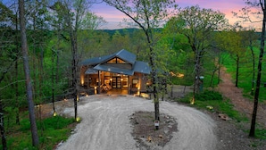 Une cabane dotée d’une grande véranda, entourée d’arbres et bordée d’un sentier de terre.
