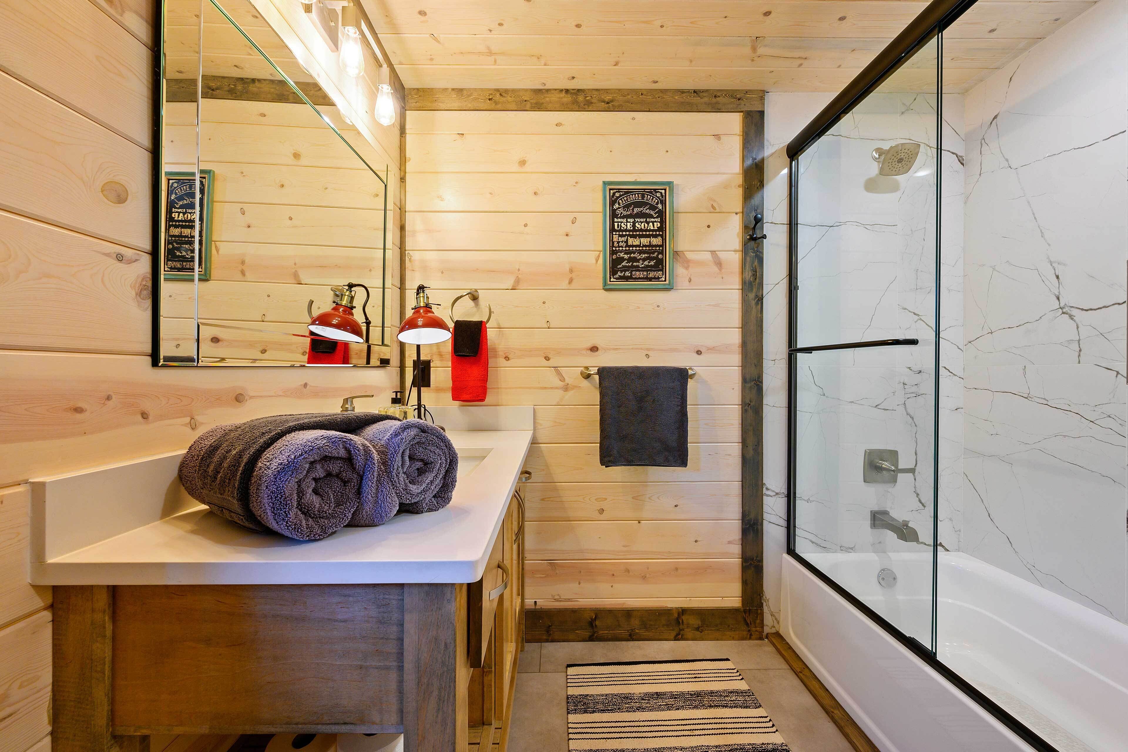 A wooden cabin bathroom with a glass shower, wooden walls, a sink with a red lamp, and a towel on the counter.