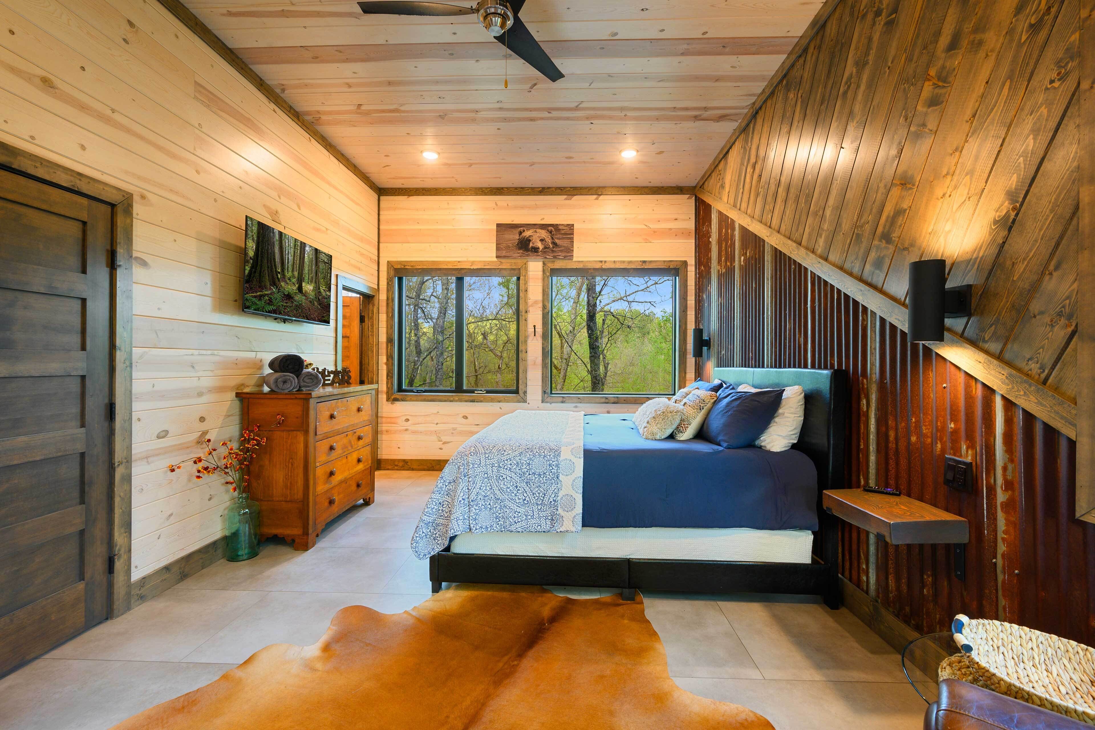 Quarto com cama, paredes de madeira, ventilador de teto, janela e cômoda de madeira.