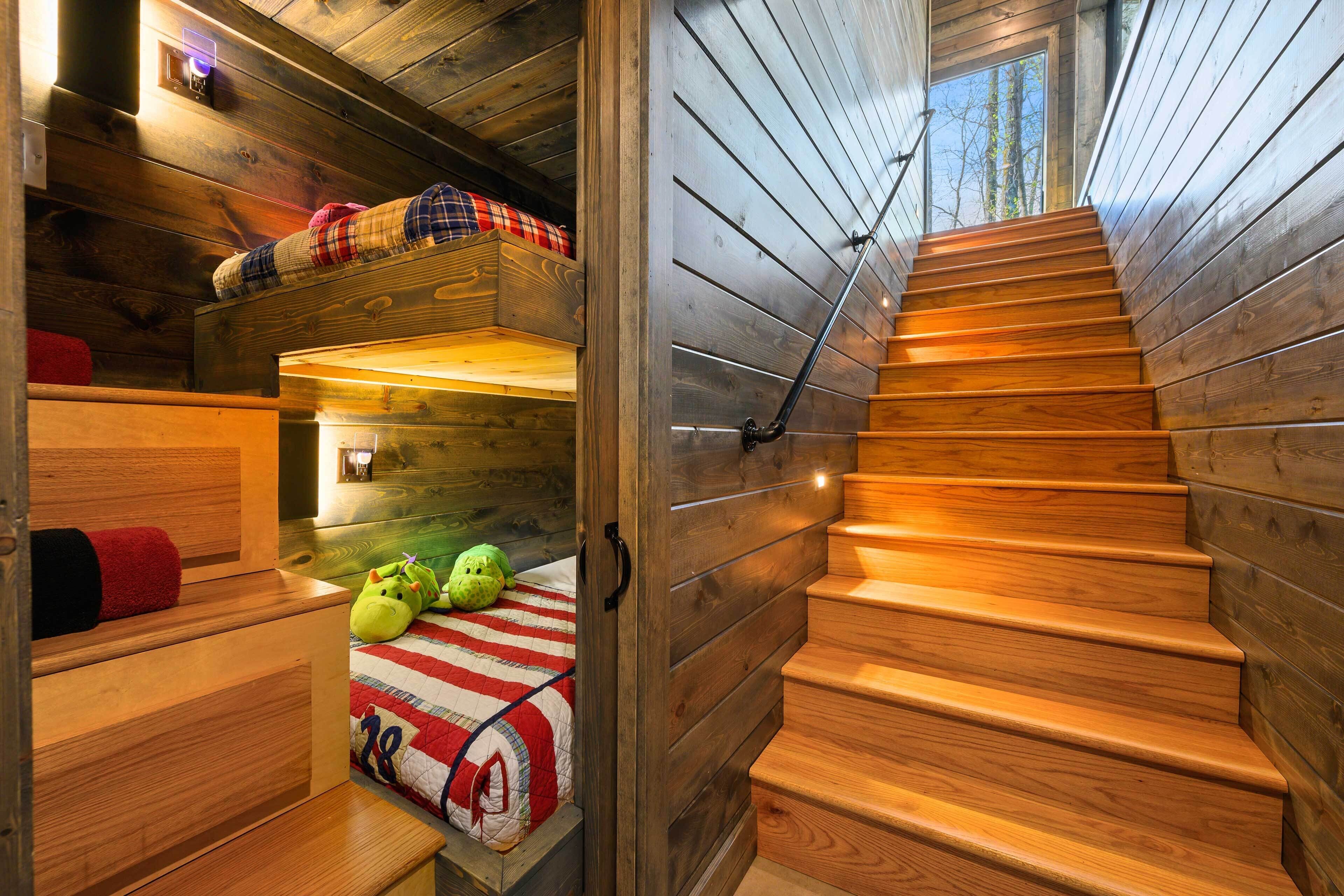 A wooden interior with a staircase, bunk beds, and a window.