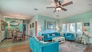 A spacious living room with a teal sofa set, a dining area with a wooden table and chairs, and a ceiling fan.