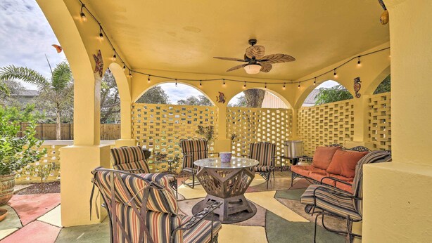 An outdoor patio with striped chairs, a round table, and a ceiling fan.