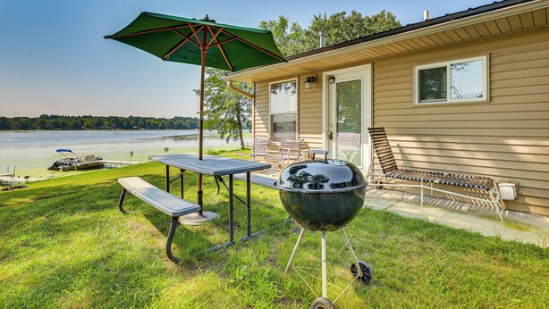 Un jardin avec un barbecue, une table de pique-nique et un parasol.