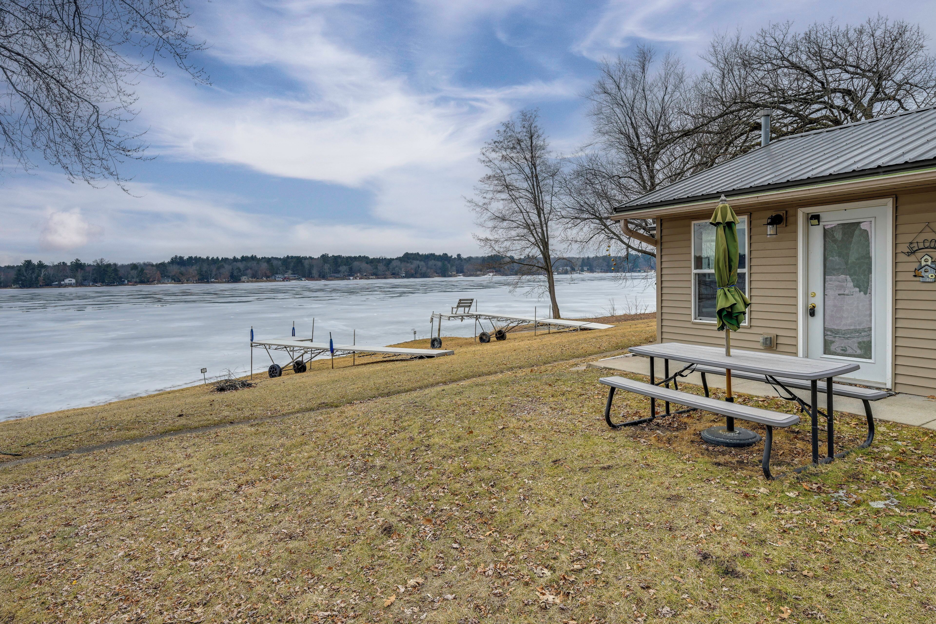 A picnic table and bench by a lakeside with a small building in the background.