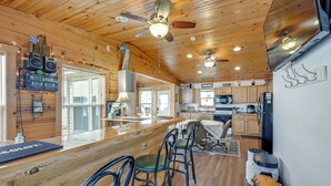 Une cuisine spacieuse avec des meubles de rangement en bois, un îlot central doté de tabourets de bar et un ventilateur de plafond.