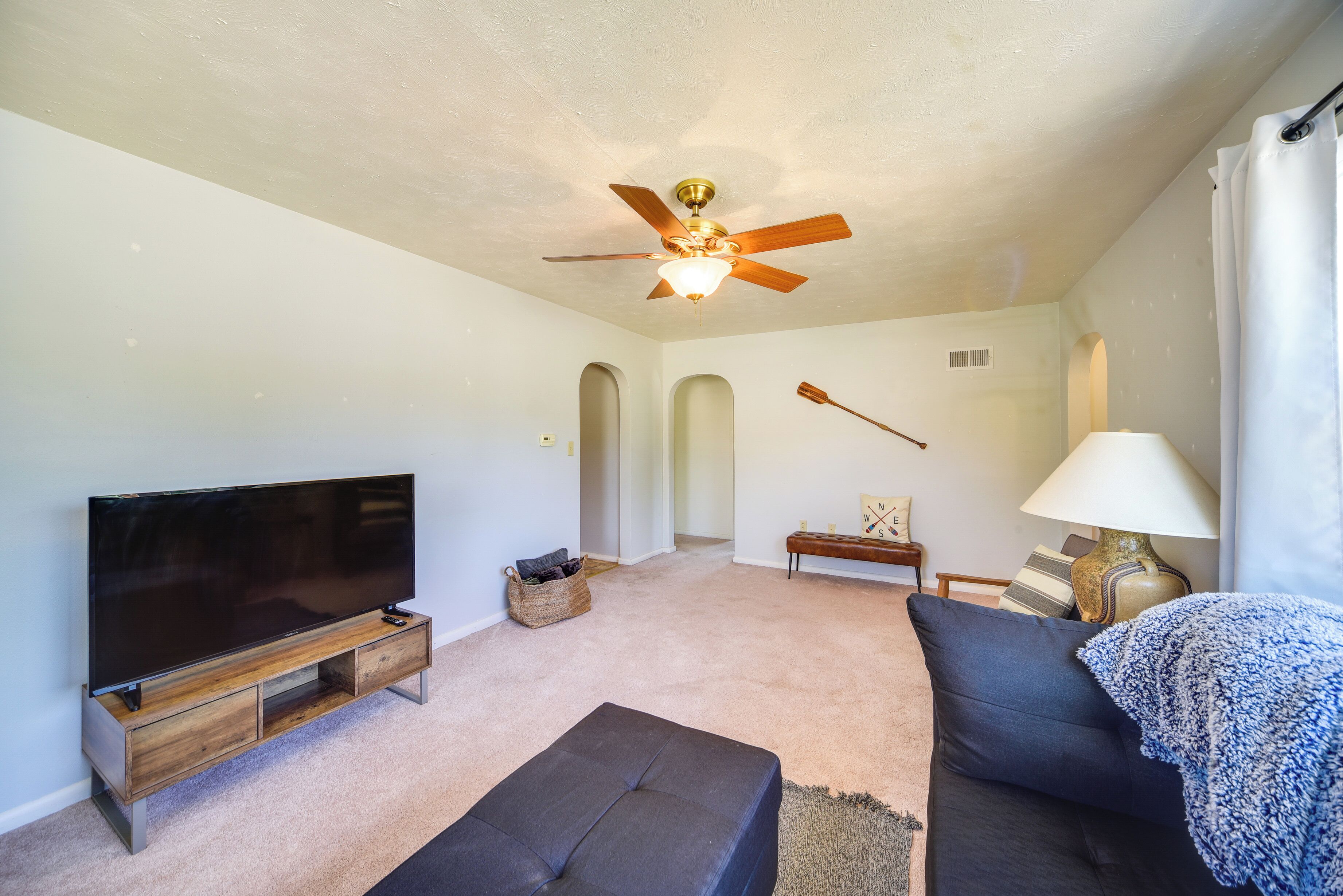 A living room with a flat-screen TV, a ceiling fan, a sofa, a lamp, and a small table.