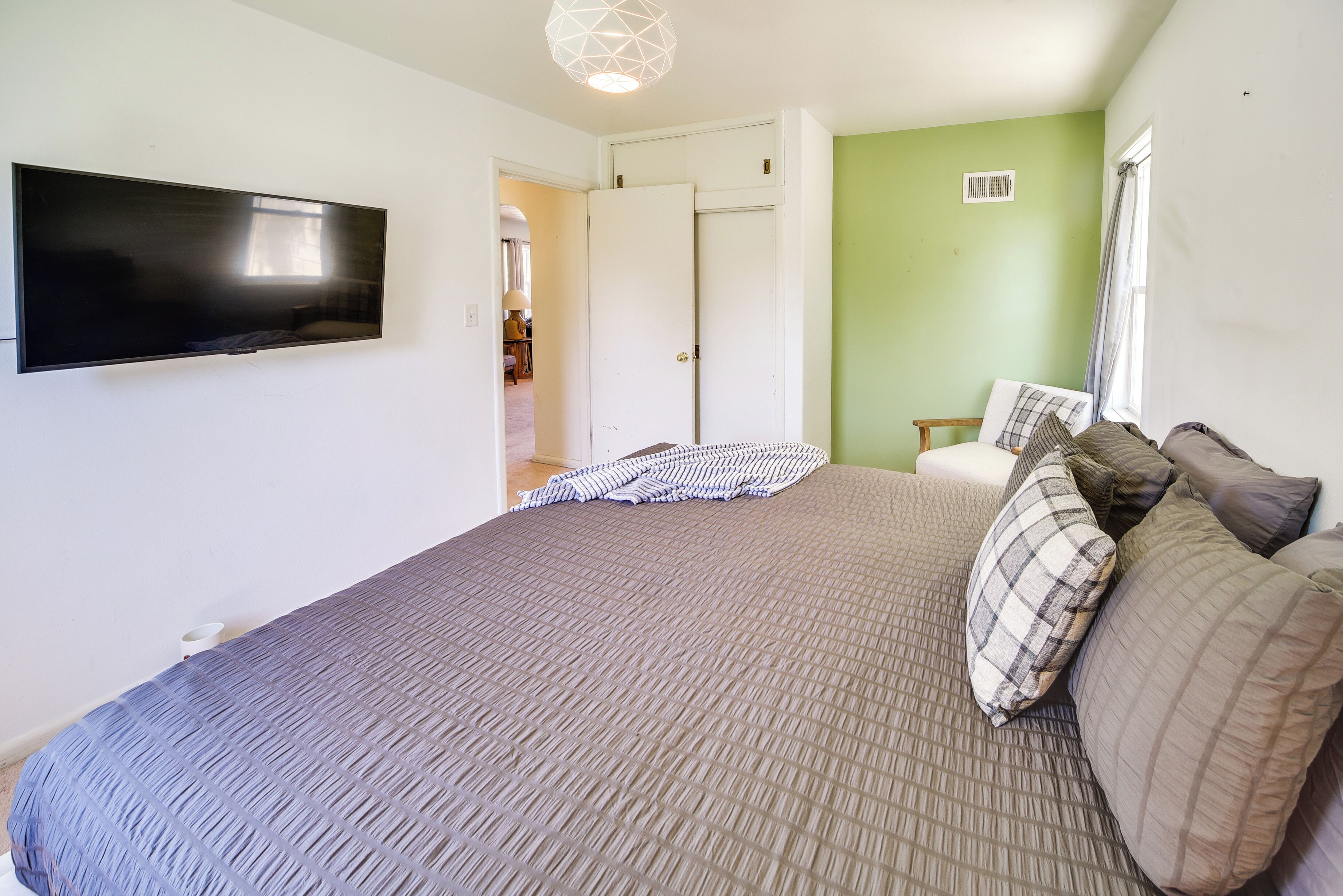 Un dormitorio con una cama grande, un televisor de pantalla plana montado en la pared y una puerta que da a otra habitación.