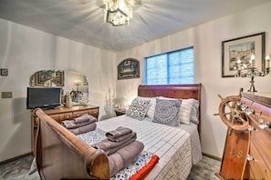 Une chambre à coucher bien rangée, avec un lit, une tête de lit en bois, une commode, un téléviseur et un élément décoratif en forme de roue de navire.