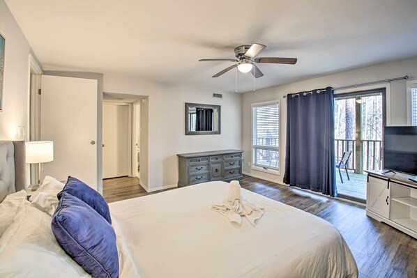 A bedroom with a bed, a ceiling fan, a dresser, a TV, and a balcony with a view.