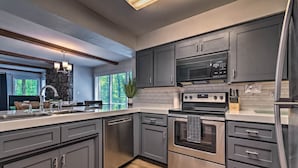 A modern kitchen with grey cabinets, stainless steel appliances, and a wooden floor. - Mount Ida Condo - Walk to Lake Ouachita! (Mount Ida)