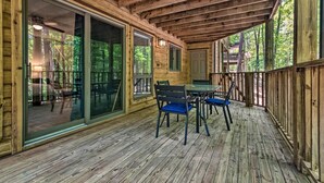 A wooden deck with a glass door leading to an outdoor area, a table with chairs, and a view of the surrounding forest. - Mount Ida Condo - Walk to Lake Ouachita! (Mount Ida)