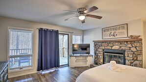 A bedroom with a bed, a TV, a stone fireplace, and a ceiling fan. - Mount Ida Condo - Walk to Lake Ouachita! (Mount Ida)