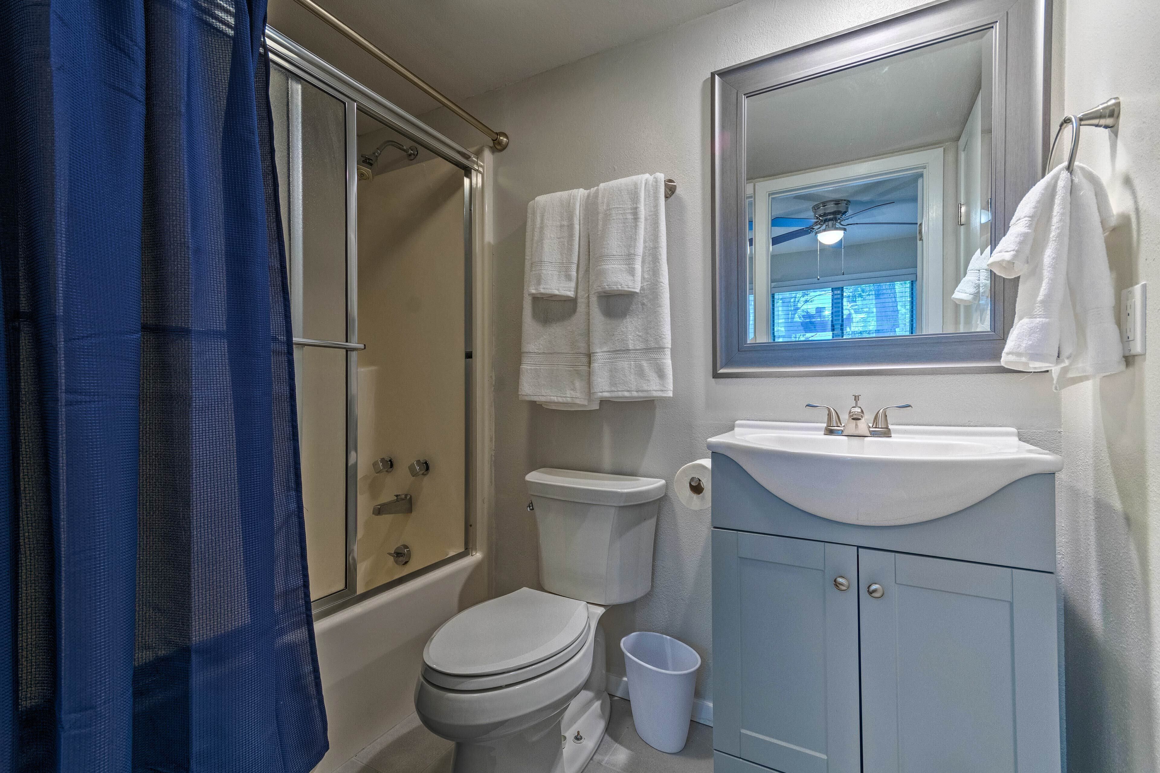 A bathroom with a shower, toilet, sink, and a mirror.