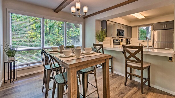 A modern kitchen with wooden flooring, a dining table with chairs, and a large window with blinds. - Mount Ida Condo - Walk to Lake Ouachita! (Mount Ida)
