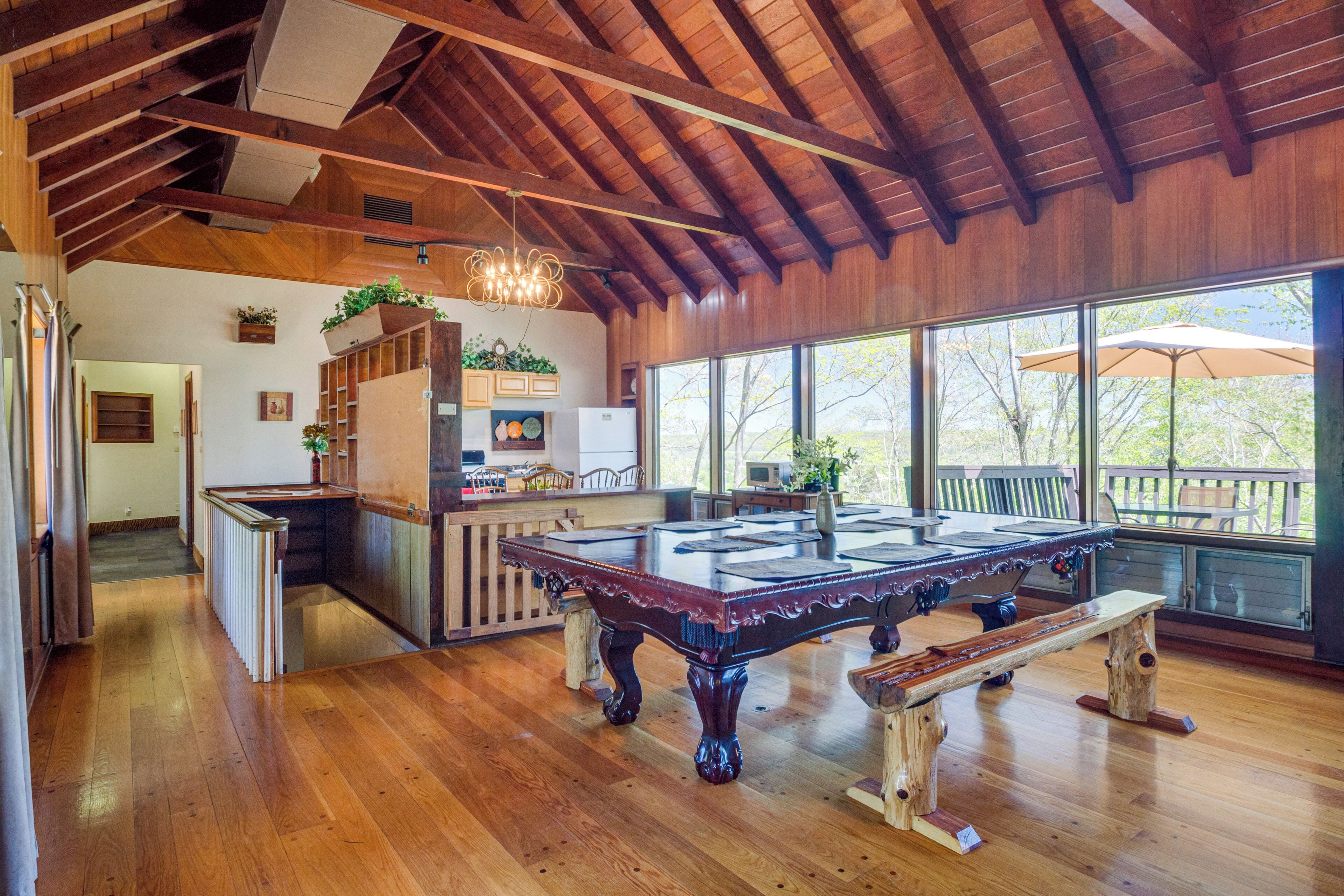 A spacious room with a wooden ceiling, a pool table, and large windows offering a view of the outdoors.