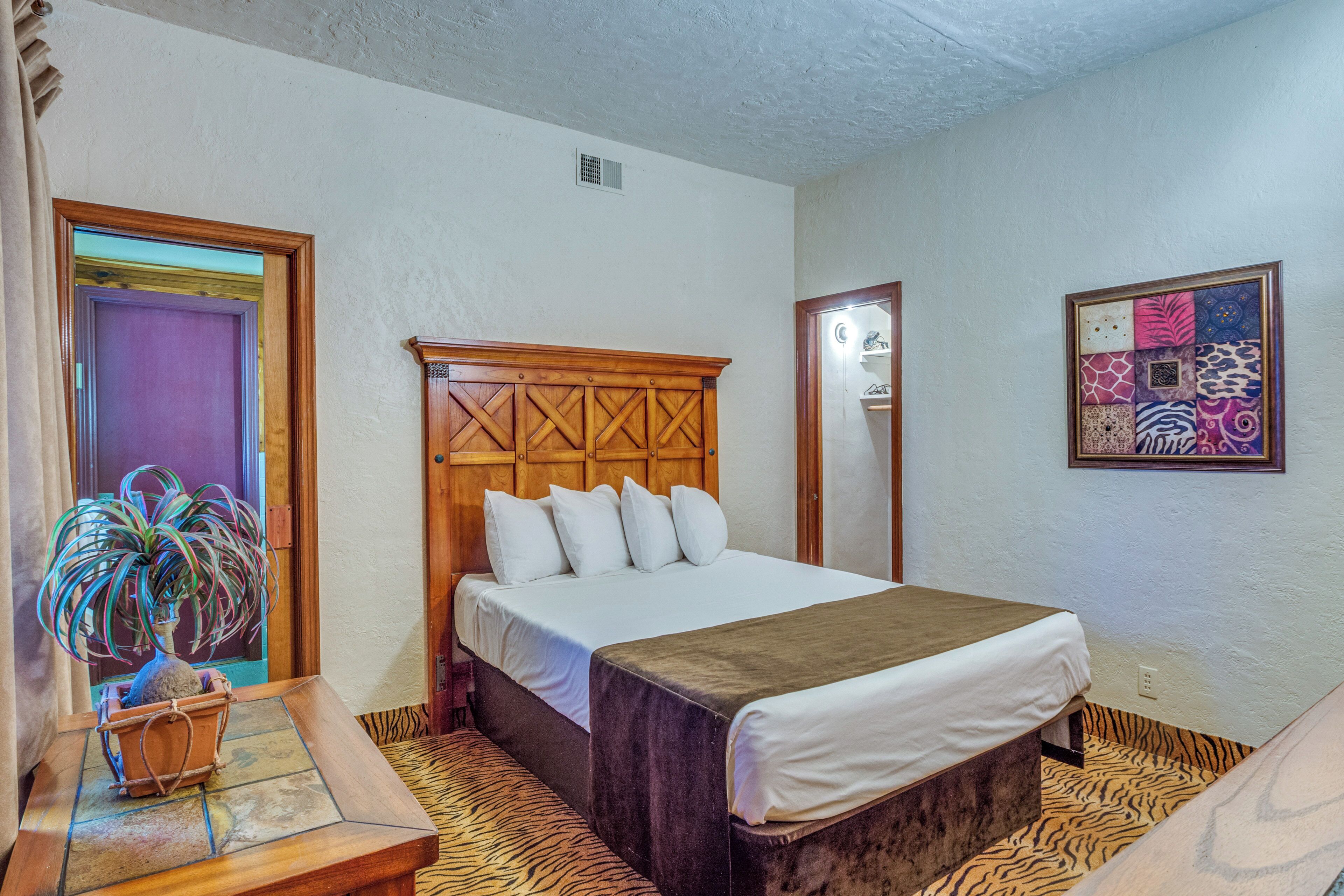 A hotel room with a large bed, a wooden headboard, a potted plant, and a zebra-patterned rug.