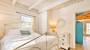 A bedroom with a metal bed frame, a white dresser, a wall clock, and a window with curtains.