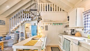 A cozy cabin-style kitchen with a wooden staircase, a dining table with chairs, and a kitchen counter with various appliances.