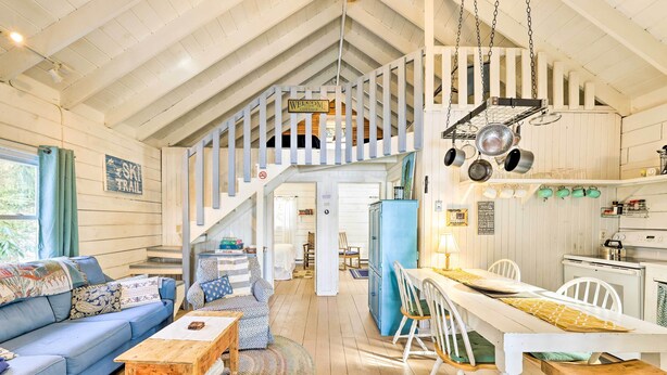 A rustic cabin interior with a wooden staircase, a dining area, and a kitchen.