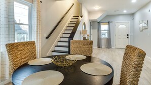 Un coin repas avec une table ronde, quatre chaises en osier, un centre de table en osier et un escalier menant à une autre pièce.