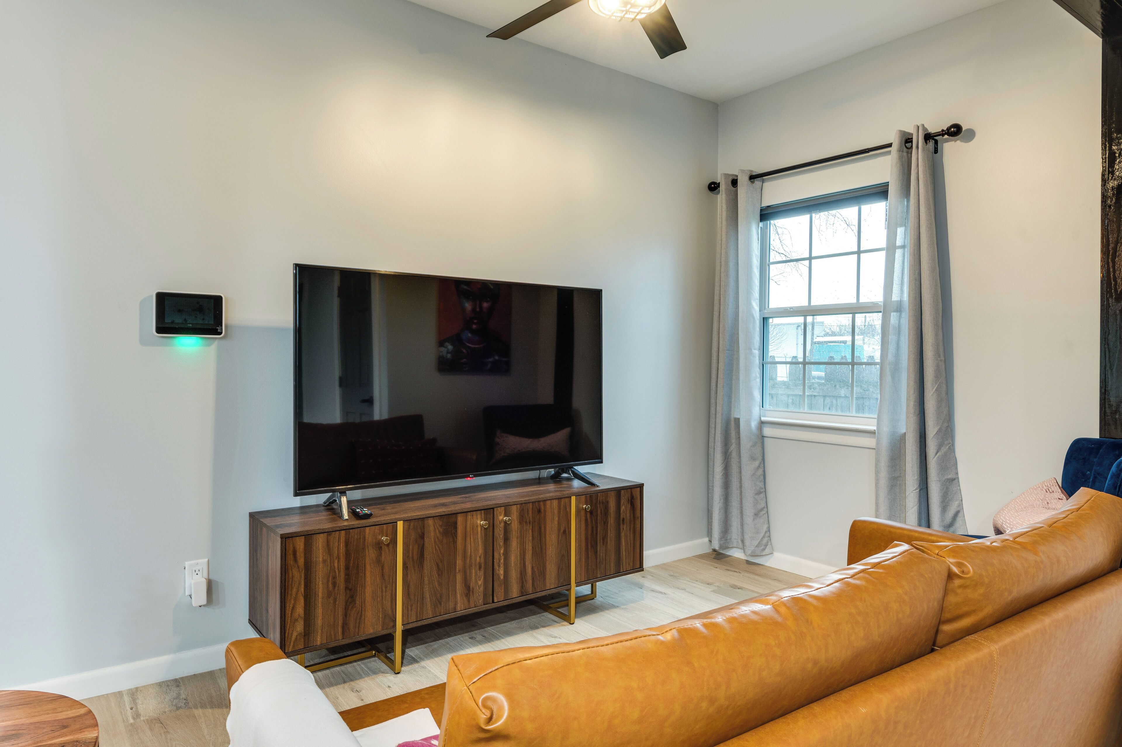 A modern living room with a flat-screen TV on a wooden cabinet, a leather sofa, and a window with curtains.