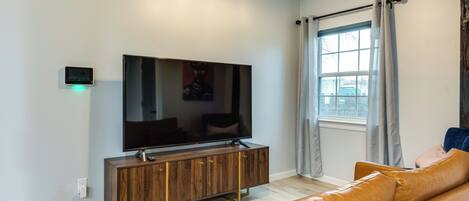 A modern living room with a flat-screen TV on a wooden cabinet, a leather sofa, and a window with curtains.