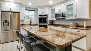 Une cuisine moderne avec des meubles blancs, des appareils en acier inoxydable, un plan de travail en bois et des tabourets de bar.