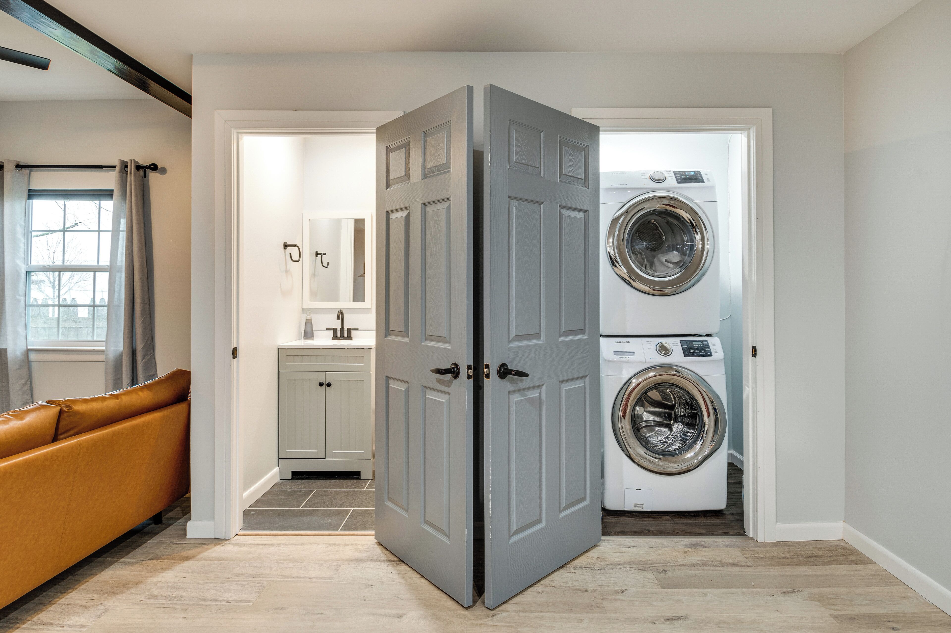 A laundry room with a washing machine and dryer, a sofa, and a door leading to another room.
