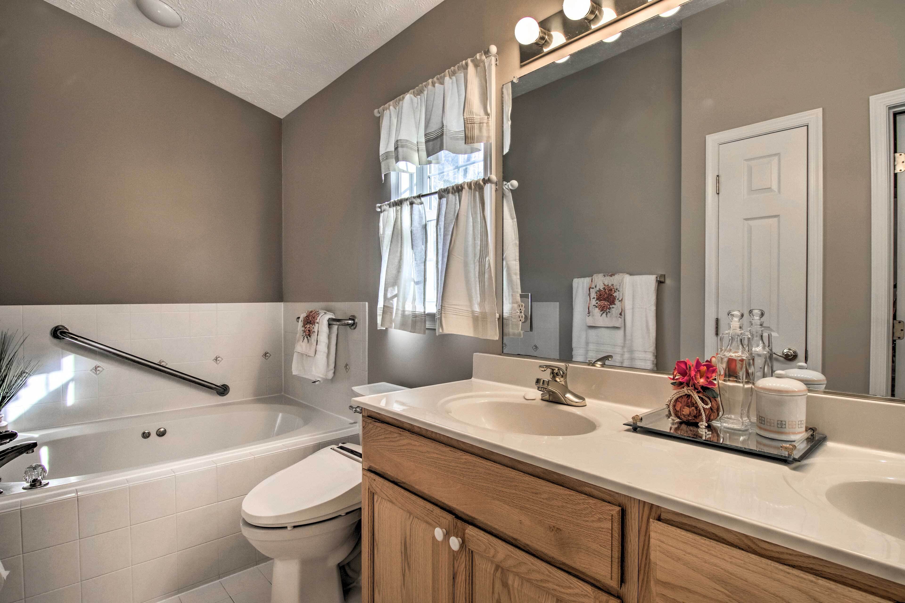 A bathroom with a bathtub, two sinks, a vanity with wooden cabinets, a mirror, and a towel rack.