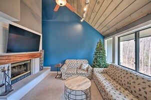 Una sala de estar acogedora con chimenea, un televisor de pantalla plana grande, techo de madera y un árbol de Navidad.