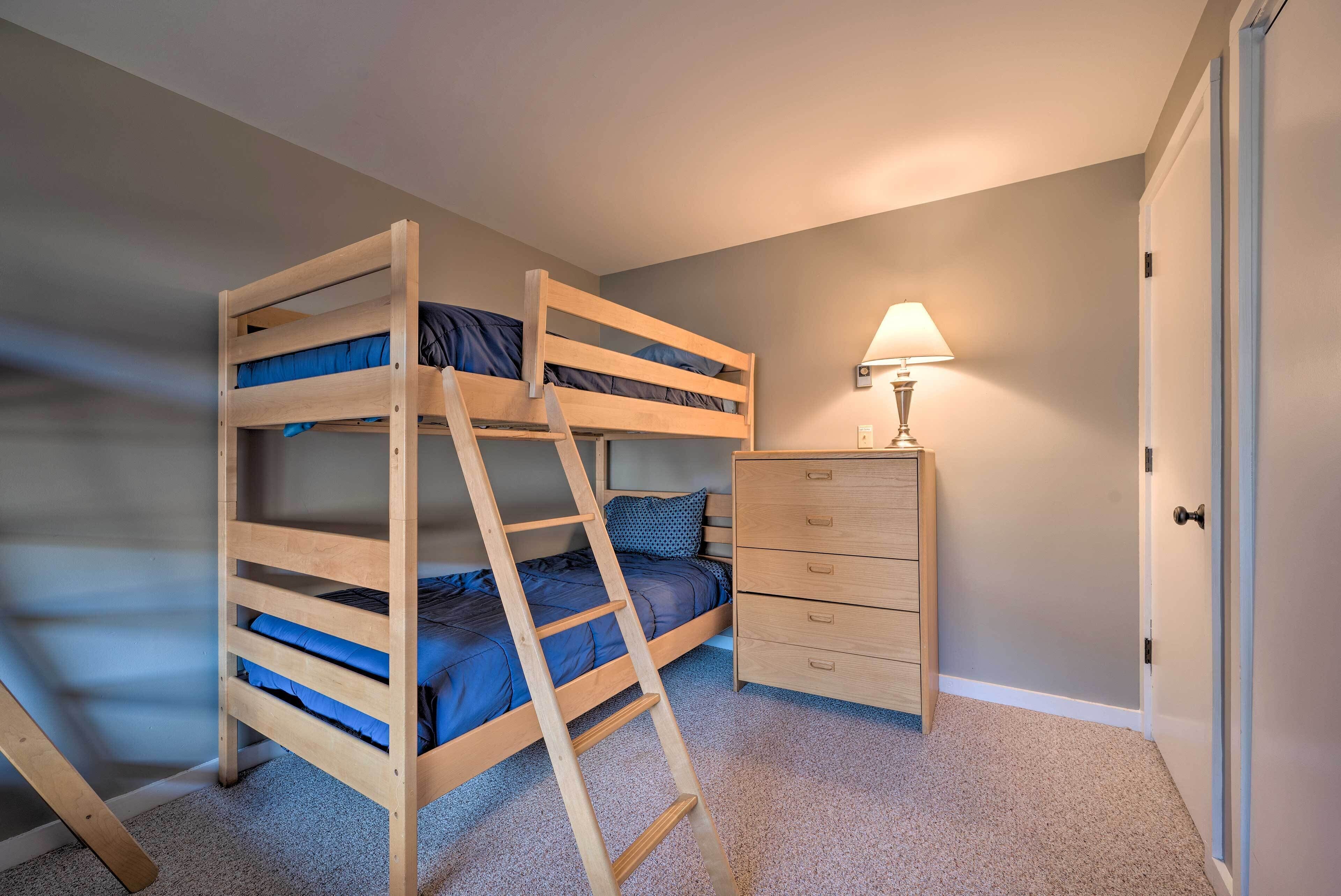 A bunk bed with a ladder, a bedside table with a lamp, and a dresser in a bedroom.