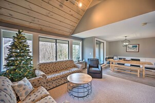 Un salón acogedor con techo de madera, un árbol de Navidad, un sofá estampado, una mesa de centro redonda y una zona de comedor con mesa y bancos de madera.