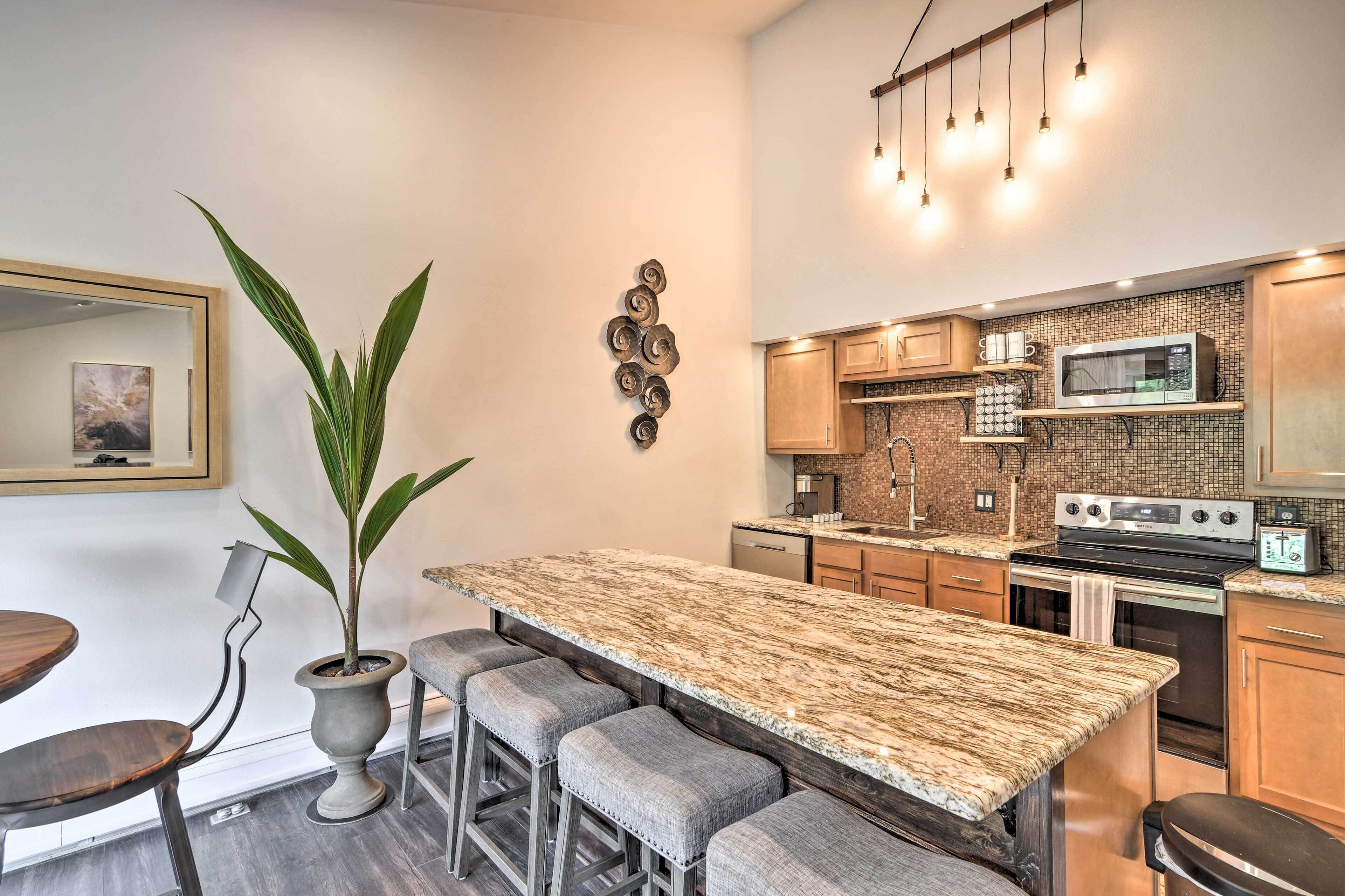 A modern kitchen with a granite countertop, stainless steel appliances, and a potted plant.