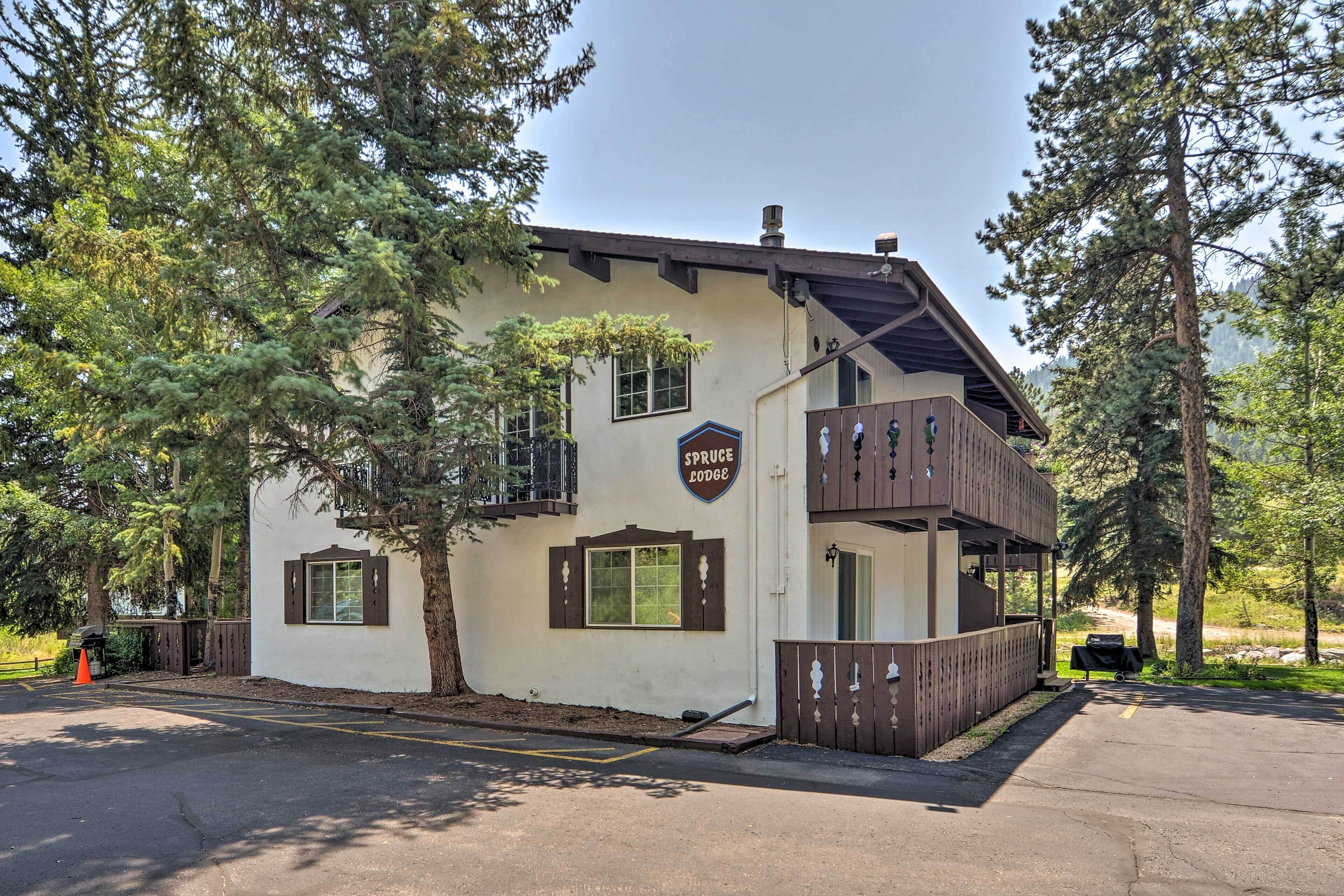 A lodge with a balcony, a sign reading "Spruce Lodge," and a barbecue grill in the parking area.