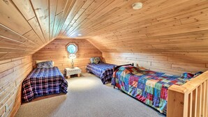 Ein gemütliches Schlafzimmer im Dachgeschoss mit Holzwänden und schrägen Decken, mit zwei Betten mit bunter Bettwäsche und einem kleinen Nachttisch mit Lampe.
