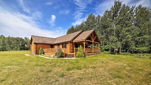 Eine Blockhütte mit Veranda und überdachter Terrasse, umgeben von einer Wiese und dichtem Wald.