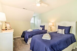 A bedroom with two beds, a ceiling fan, a nightstand with a lamp, and a dresser with a framed picture.