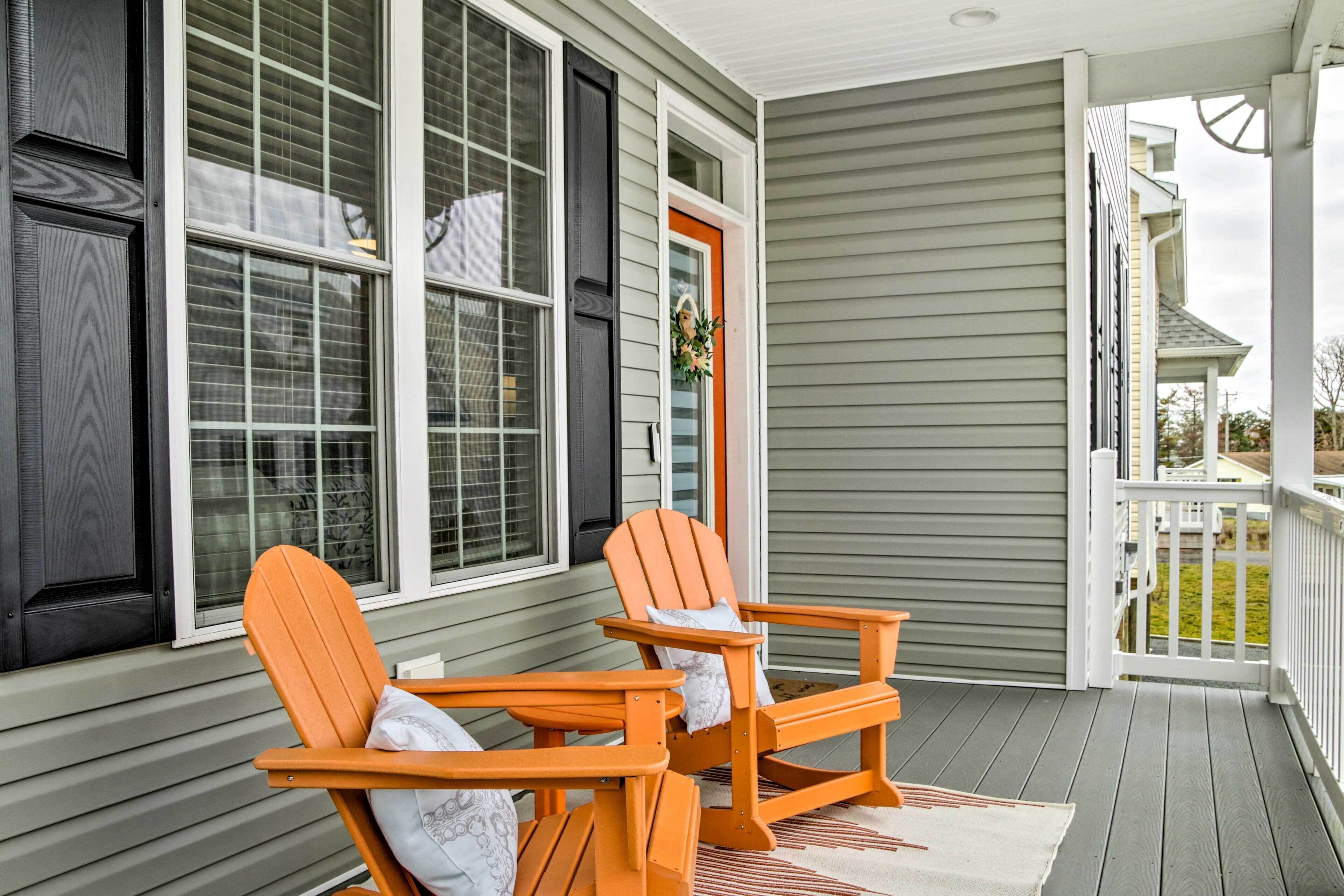 A porch with two wooden Adirondack chairs and a door with a wreath.