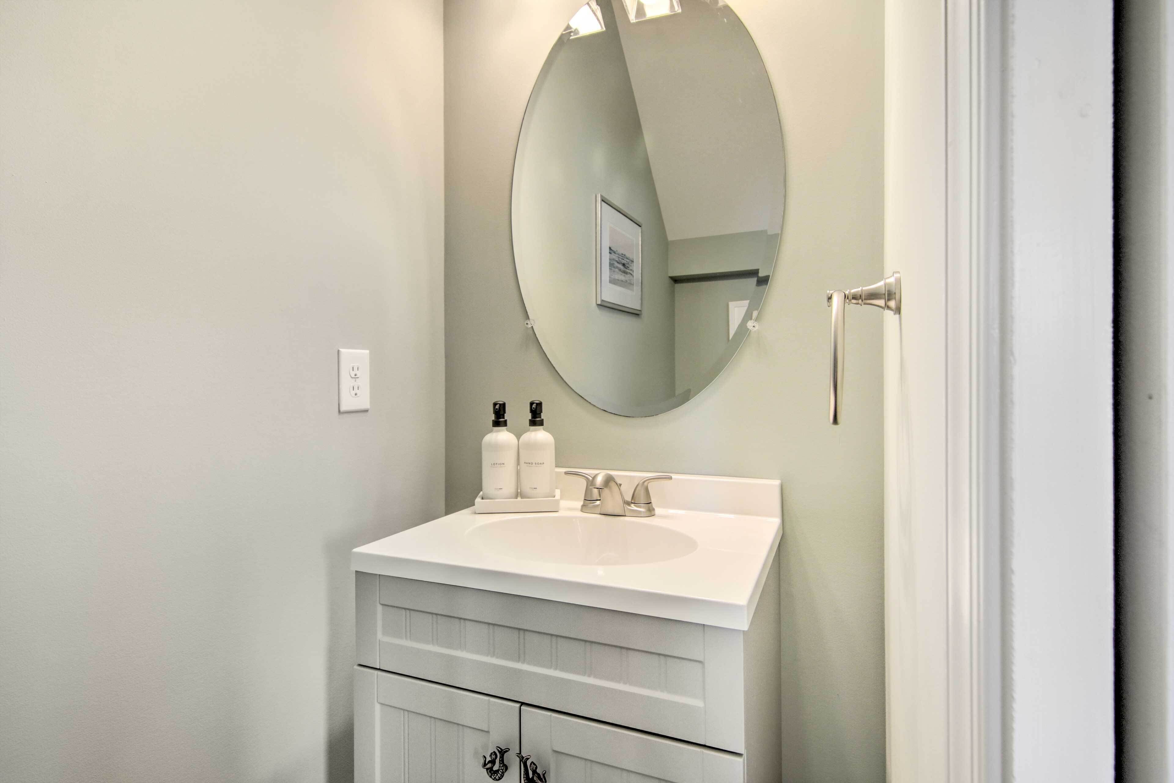 A bathroom with a white vanity, a round mirror, and two bottles of lotion on the sink.