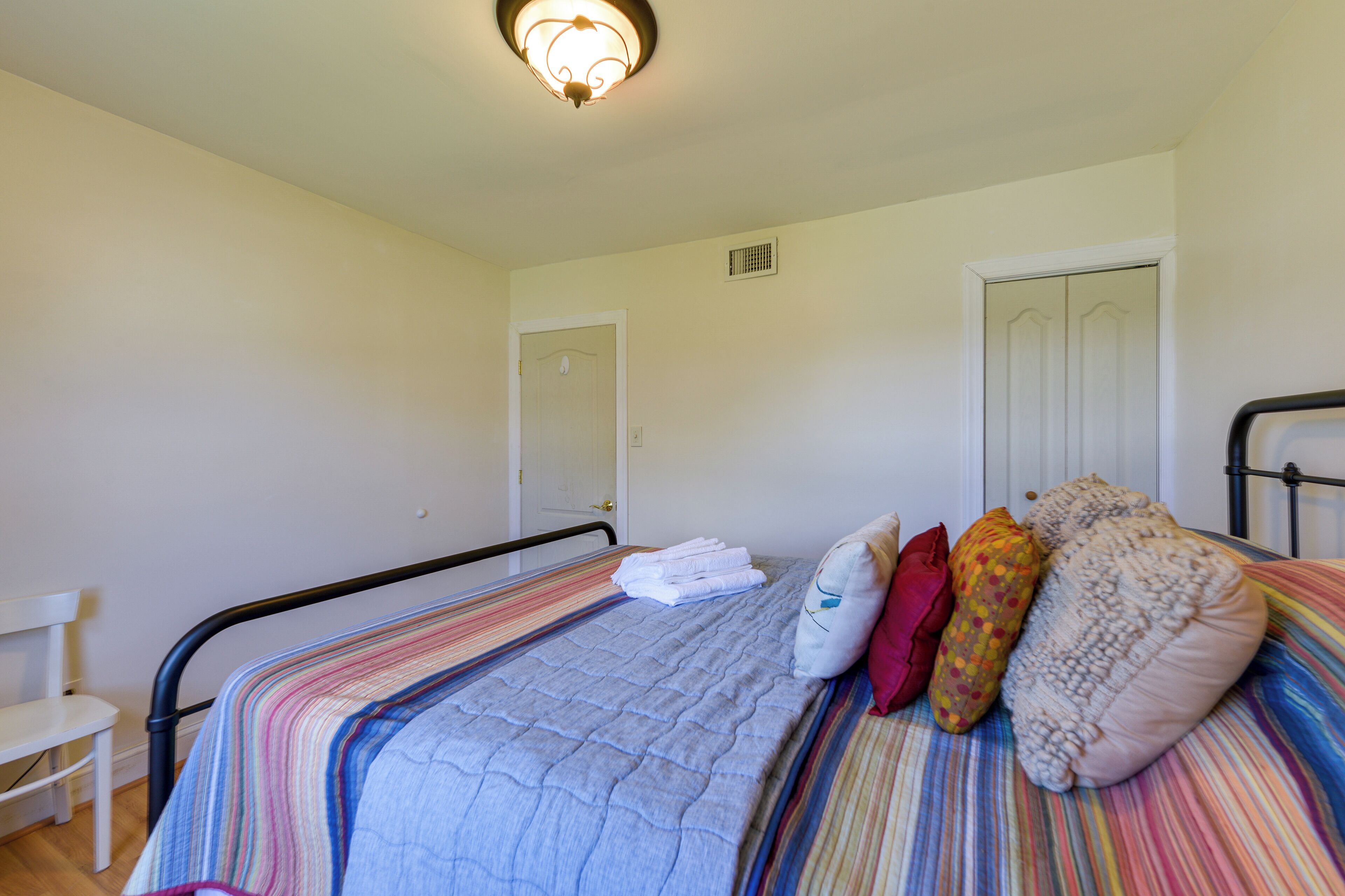 A single bed with a striped bedspread, a white chair, and a door in the background.
