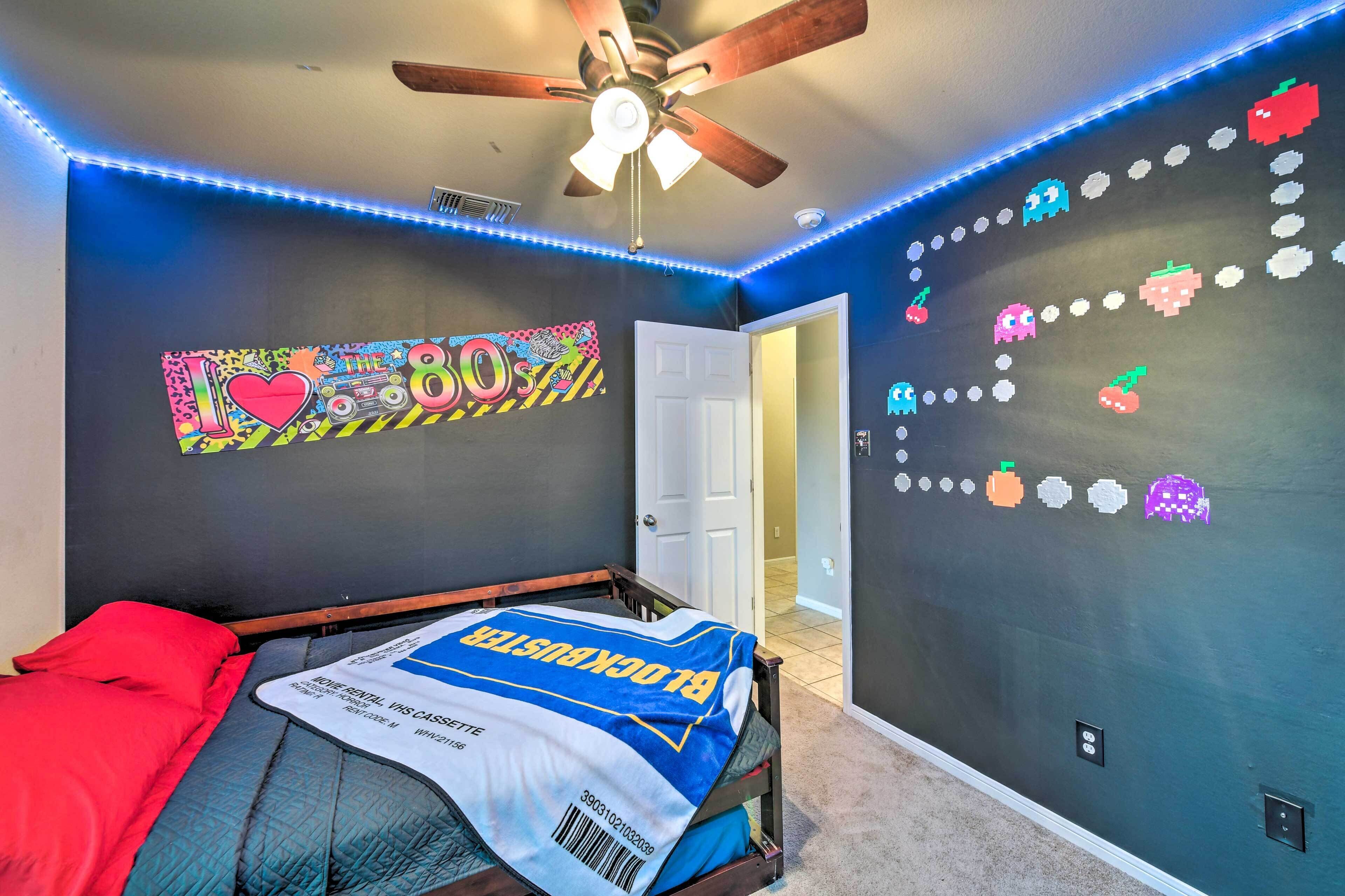 A bedroom with a bed, a ceiling fan, and a wall with a retro-themed design.