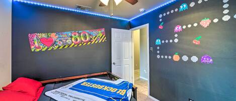 A bedroom with a bed, a ceiling fan, and a wall with a retro-themed design.