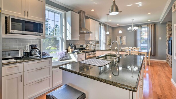 A modern kitchen with white cabinets, a large island with a sink, and a dining area with a table and chairs. - Quaint Ligonier Family Home - 3 Miles to Idlewild! (Ligonier)