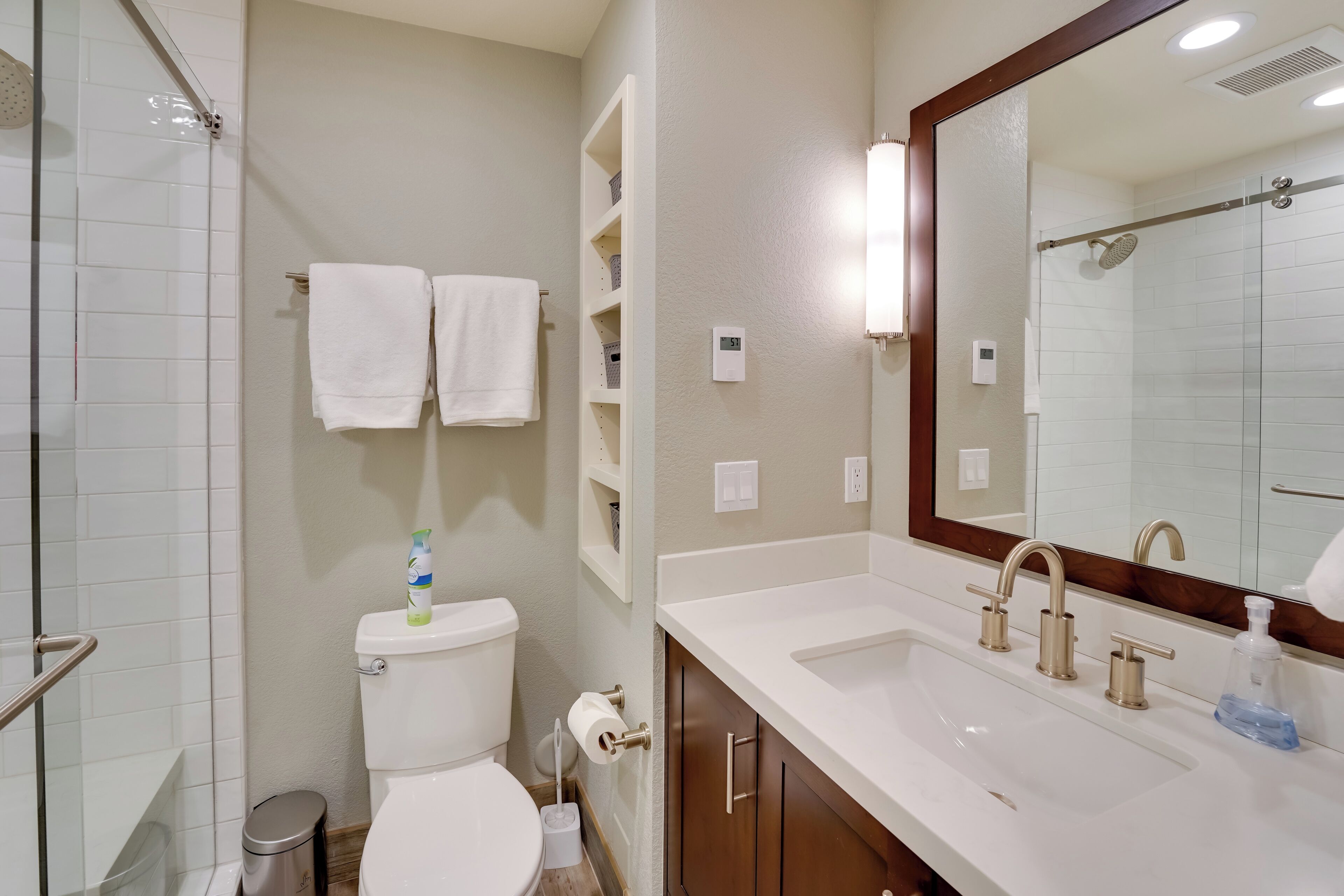 A bathroom with a toilet, sink, and shower. There are white towels hanging on a rack, a soap dispenser, and a mirror above the sink.