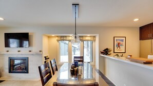 A modern kitchen with a large island, built-in appliances, and a dining area with a glass-top table and chairs. - Ski-in/out Sun Valley Condo: First-floor Unit! (Ketchum)