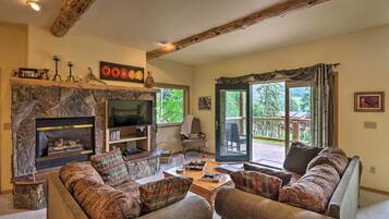 A cozy living room with a stone fireplace, comfortable seating, and a large window offering a view of the outdoors.