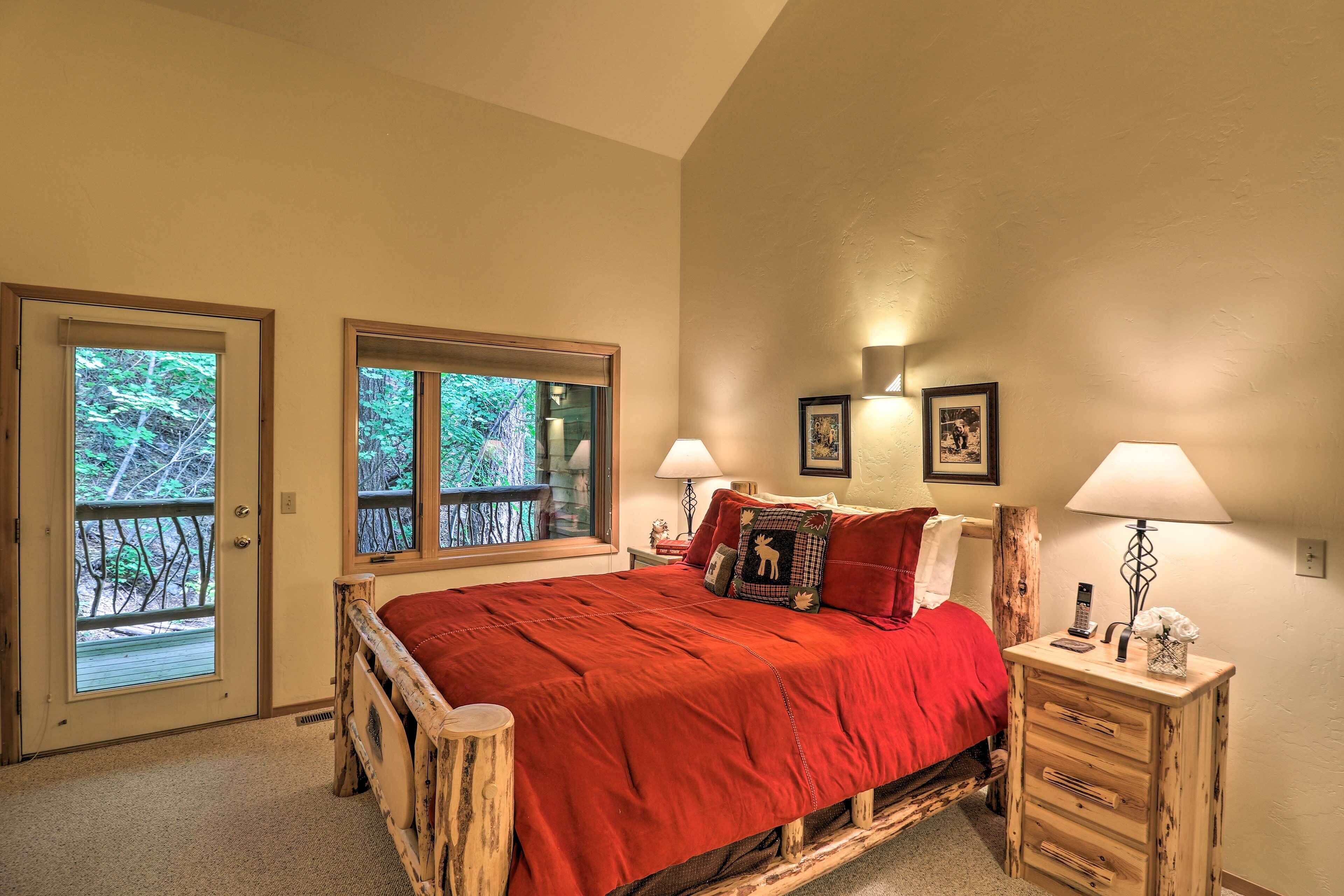 A bedroom with a wooden bed, two windows, a nightstand with a lamp, and a door leading to an outdoor area.