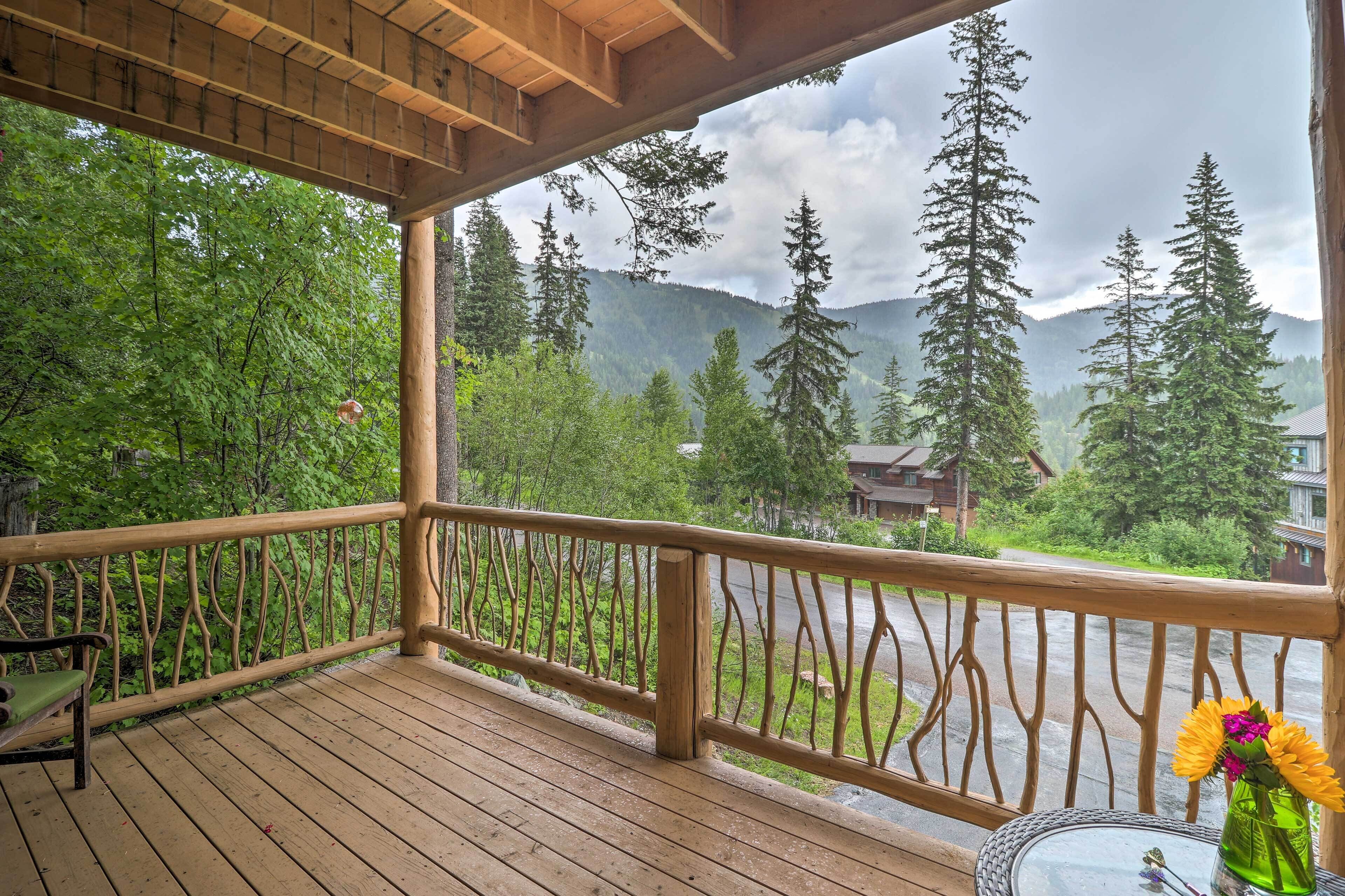 A wooden deck with a railing, a bench, and a table with a vase of flowers.