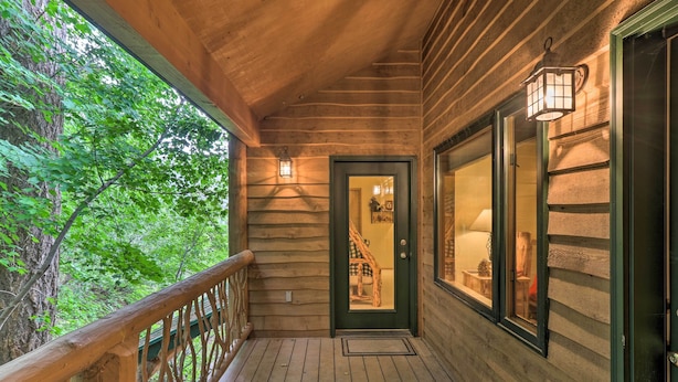 Une véranda en bois avec une balustrade, une porte donnant sur l’intérieur et une vue sur les arbres environnants.