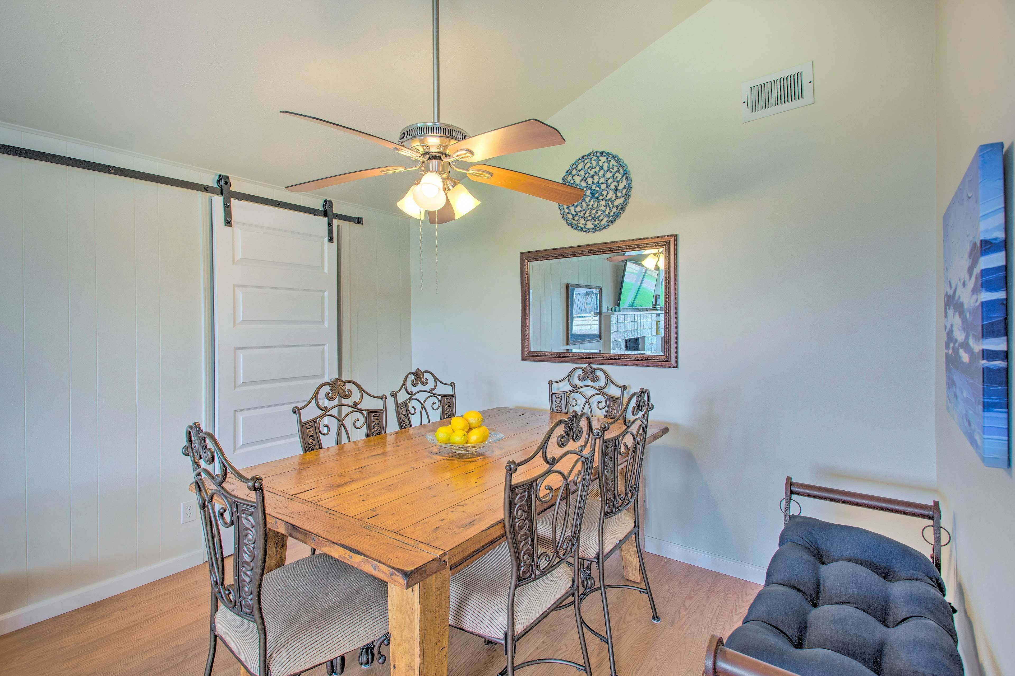 A dining area with a wooden table, six chairs, a ceiling fan, and a small sofa.